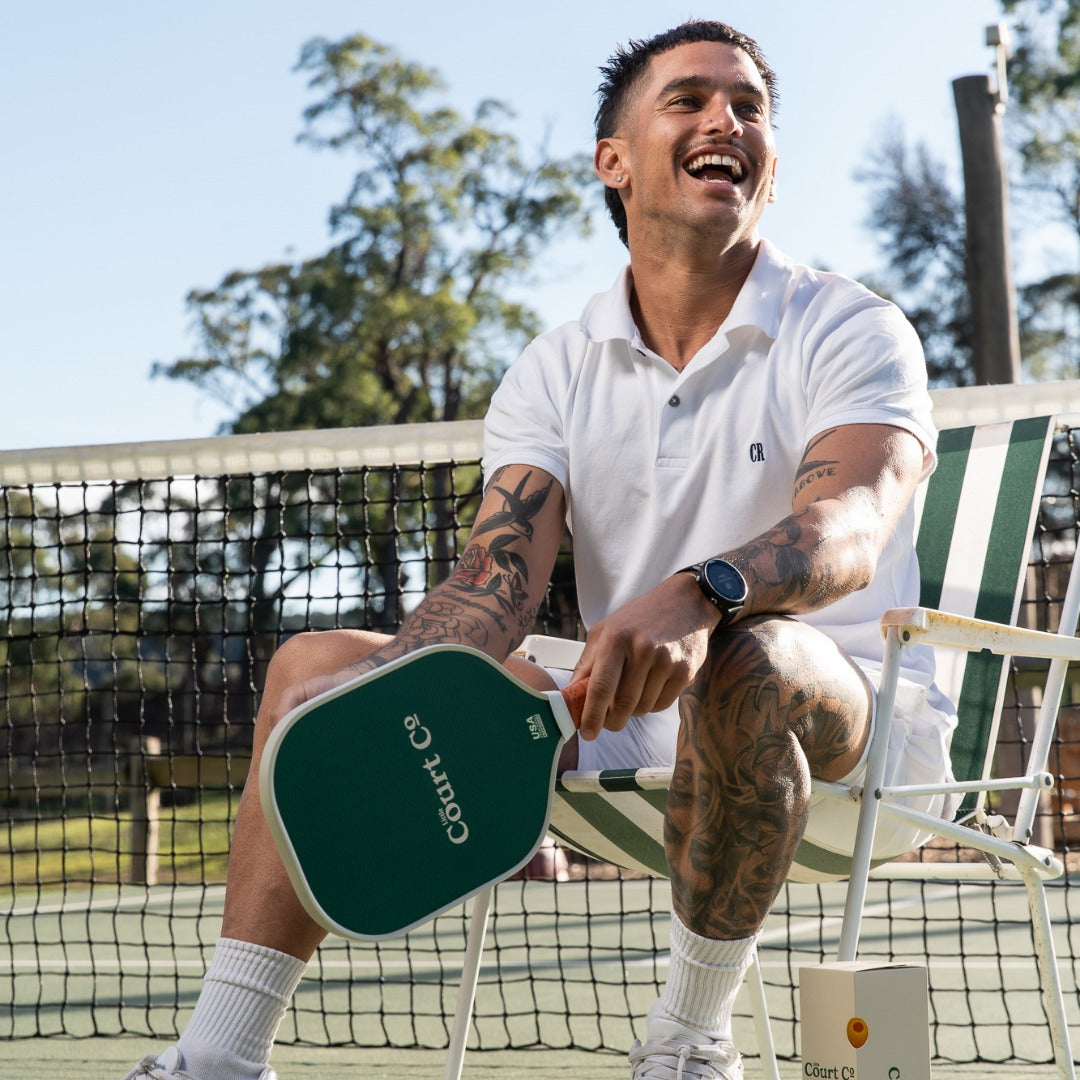 Man sitting on a chair holding a pickleball paddle on a tennis court